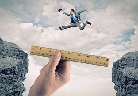 Young businessman in suit jumping over mountain gapの写真素材