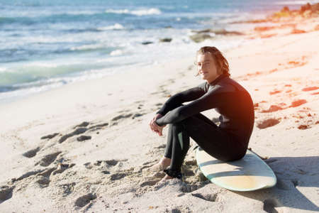 A young man sitting on his surfboard on the sandの写真素材