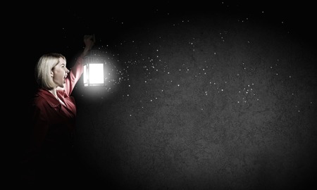 Young blonde in red cloak with lantern in darknessの写真素材