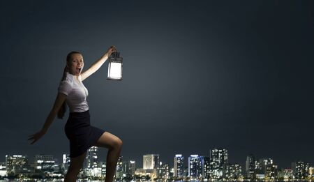 Young businesswoman walking in darkness with lantern in handの写真素材