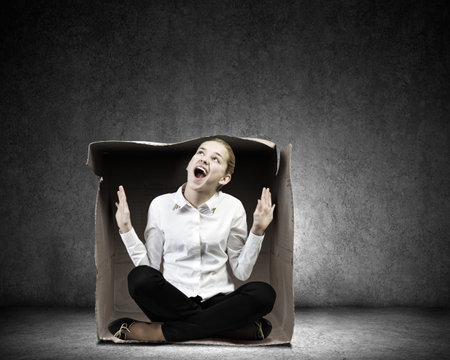 Young businesswoman sitting in carton box and feeling uncomfortable