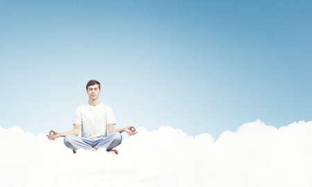 Young smiling guy sitting on cloud and meditatingの写真素材
