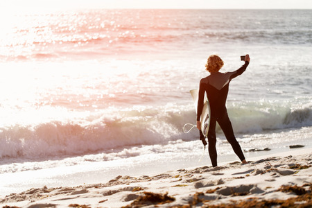 A surfer with his surfboard at the beach doing selfieの写真素材