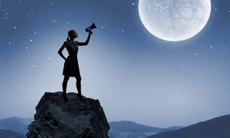 Silhouette of woman on top of rock screaming in megaphoneの写真素材