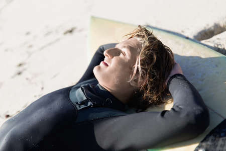 A surfer relaxing and lying on his surfboard at the beachの写真素材