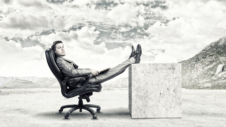 Young confident businessman sitting in chair with book in handsの写真素材