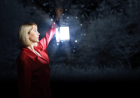 Young blonde in red cloak with lantern in night forest