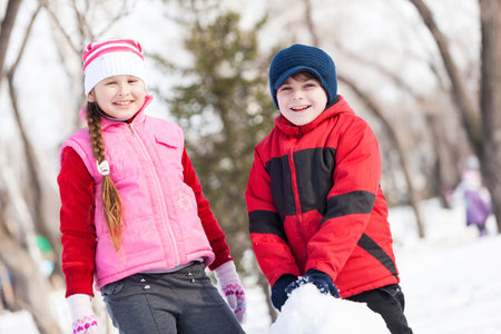 Cute boy and girl building snowman in winter parkの写真素材