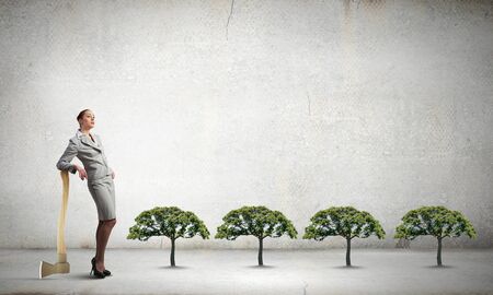 Young businesswoman with axe and green treeの写真素材