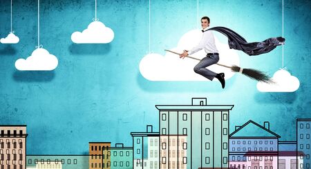 Young businessman flying on broom high in skyの写真素材
