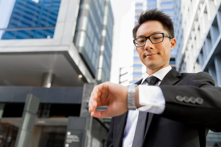 Businessman standing in street and looking at his watchの写真素材