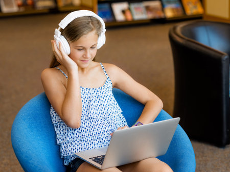 A teenage girl with headphones sitting in a library