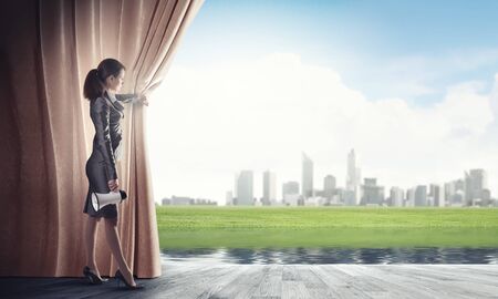 Young businesswoman opening stage curtain to another realityの写真素材