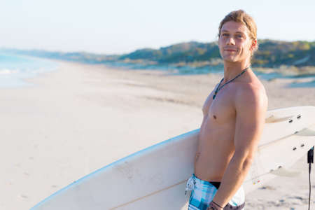 A young surfer with his board on the beachの写真素材