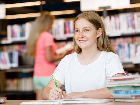 Teenage girl with books studying in libraryの写真素材