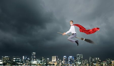 Young businessman flying on broom high in skyの写真素材