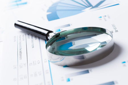 Magnifing glass and documents with analytics data lying on table