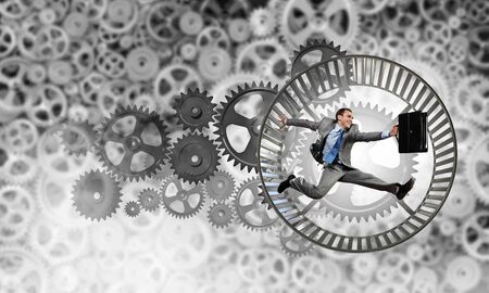 Young businessman running in wheel of gears mechanismの写真素材
