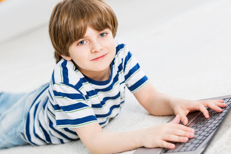 Cute boy lying on floor and using laptop