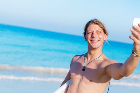 A young surfer taking his selfie on the beachの写真素材