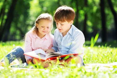 Sister and brother in the park reading a bookの写真素材