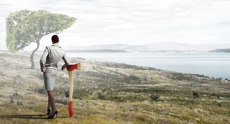 Young businesswoman with axe and green treeの写真素材