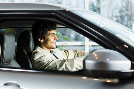 Handsome young man sitting in car in showroom
