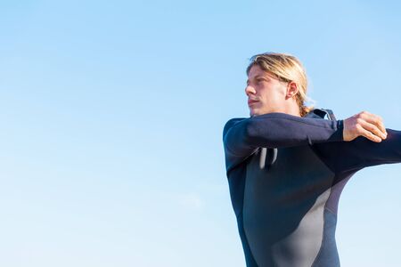 A young surfer putting on his wetsuit on the beachの写真素材