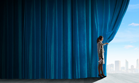 Young woman in business suit opening color curtain of stageの写真素材