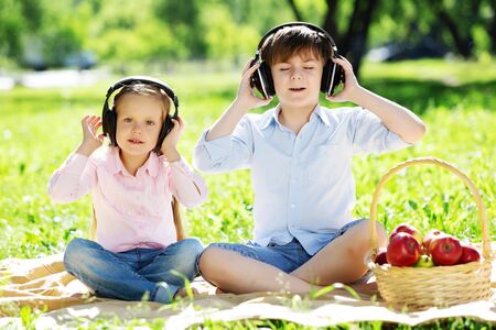 Cute boy and girl in summer park listening to musicの写真素材