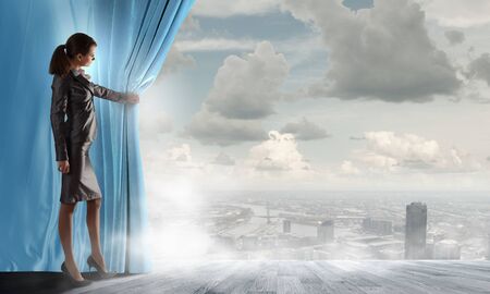Young businesswoman opening stage curtain to another realityの写真素材