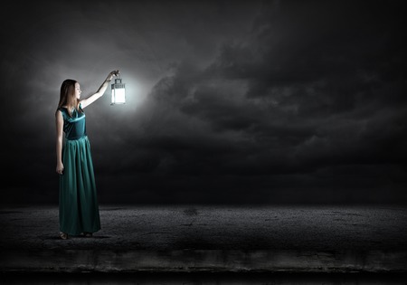 Young woman with lantern walking in darknessの写真素材