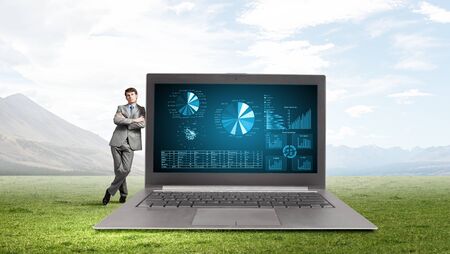 Young businessman leaning on laptop of big sizeの写真素材