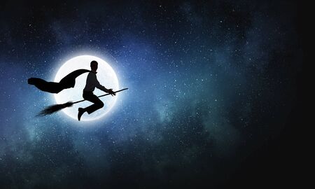 Young businessman flying on broom high in skyの写真素材