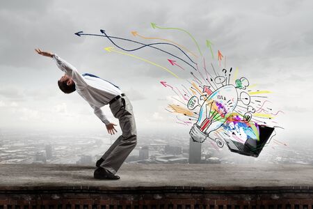 Young businessman evading colorful splashes flying from laptopの写真素材