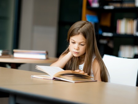 Little girl reading books in libraryの写真素材