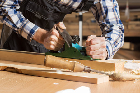 Close up of carpenter hands working with plane in his studio