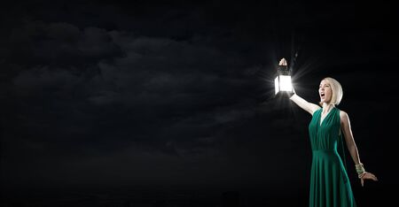 Young woman in green dress with lantern in darknessの写真素材