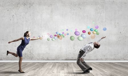 Young businessman trying to evade from thrown colorful balloonsの写真素材