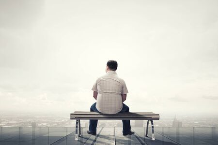 Fat man sitting on bench with his back and looking awayの写真素材