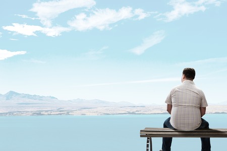 Fat man sitting on bench with his back and looking awayの写真素材
