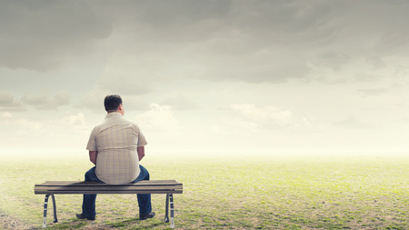 Fat man sitting on bench with his back and looking awayの写真素材