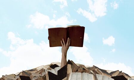 Hand with book reaching out from pile of old booksの写真素材