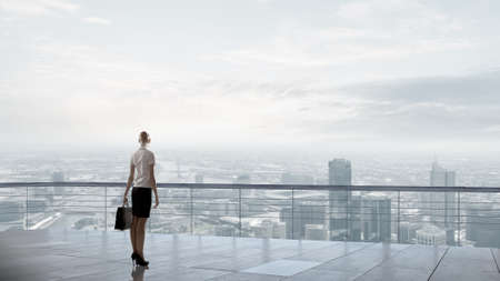 Back view of businesswoman standing on roof looking at cityの写真素材