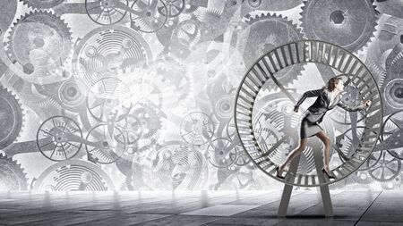 Young businesswoman running in wheel of gears mechanismの写真素材