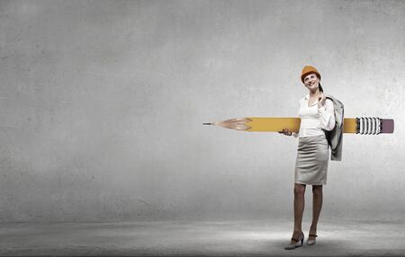 Young female engineer in hard hat with big pencilの写真素材
