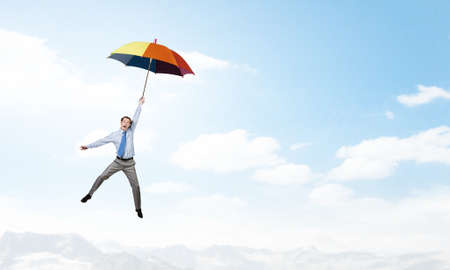 Young businessman flying high in sky on umbrellaの写真素材