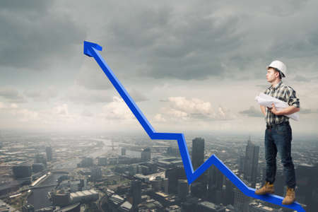 Young man builder standing on graph and looking at cityの写真素材