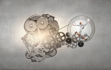 Young businesswoman running in wheel of gears mechanismの写真素材