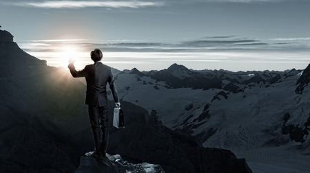 Rear view of businessman look at sunrise above mountainの写真素材